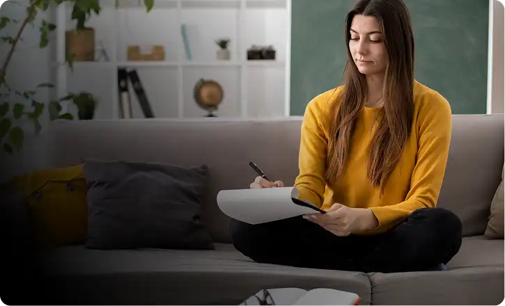 A woman writing in a notebook in a comfortable home setting